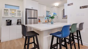Una cocina moderna con armarios blancos, un refrigerador de acero inoxidable, una cafetera y un florero con flores en la isla.