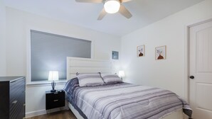 Un dormitorio con cama, lámparas de noche, ventilador de techo, ventana con persianas y puerta.