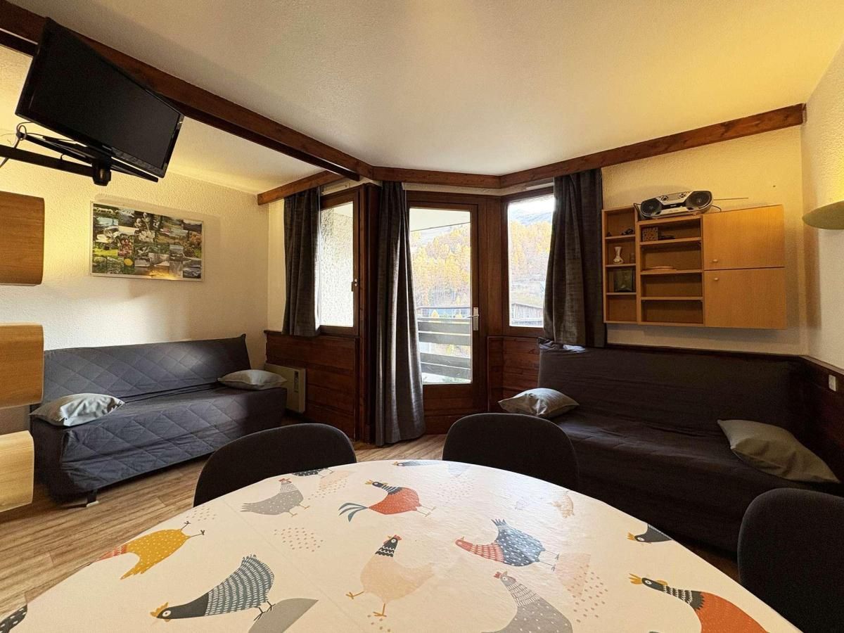 A cozy room with a round table, two sofas, a TV, and a window with curtains.