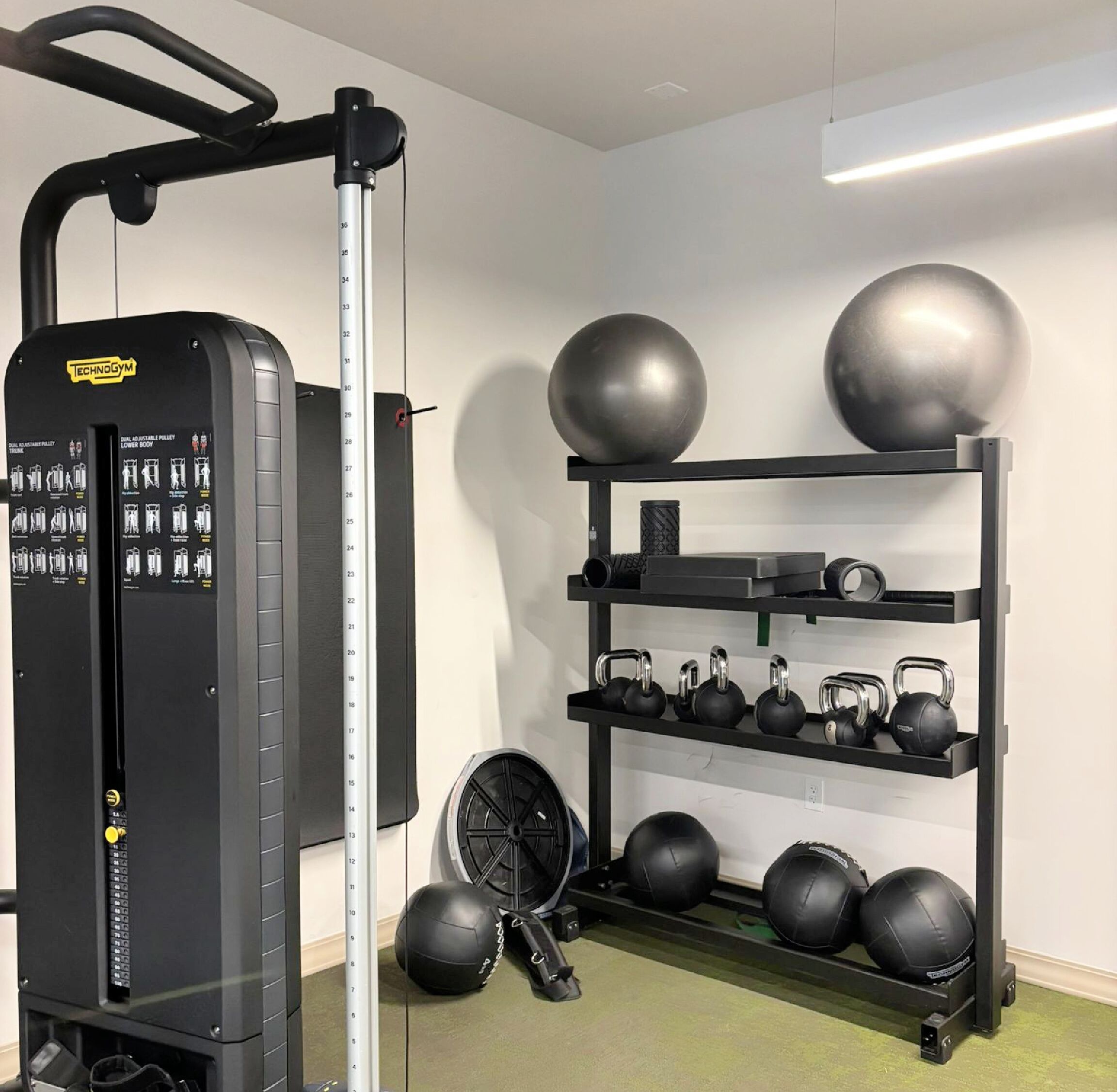 A gym with a weight machine, kettlebells, and exercise balls.