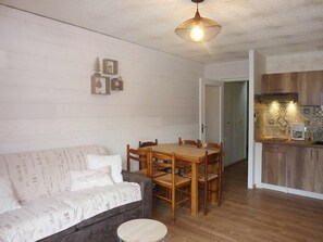 A cozy living room with a sofa, wooden dining table, and chairs. A kitchen is visible in the background with wooden cabinets and a stove. - Ski-in/ski-out & foot of the slopes, 8th floor, view valley/mountain, balcony, tv, 31m², Les Orres (Les Orres)