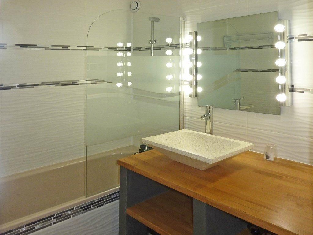 Ein Badezimmer mit Duschkabine aus Glas, einem hölzernen Waschtisch mit weißem Waschbecken und einem großen Spiegel mit Beleuchtung.