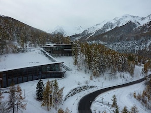 A modern building with large windows and a curved driveway, surrounded by snow-covered trees and mountains.