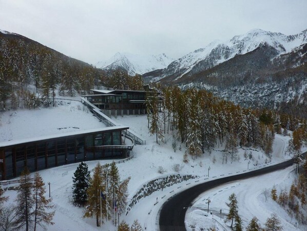 A modern building with large windows and a curved driveway, surrounded by snow-covered trees and mountains.