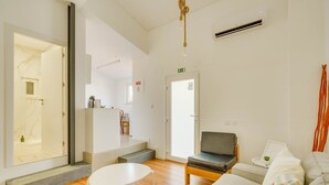 A modern living room with a sofa, a small table, and a chair. There is a staircase leading to another room, and a door with an exit sign.