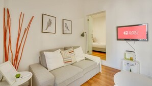 A modern living room with a sofa, a small table with a lamp, and a TV displaying "GUEST READY".