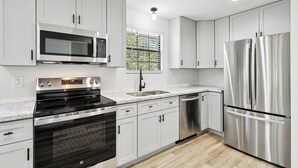 A modern kitchen with stainless steel appliances, white cabinetry, and a window with blinds. - Waterfront 2BR/1BA – Fully Furnished Home in Covington, LA (Covington)