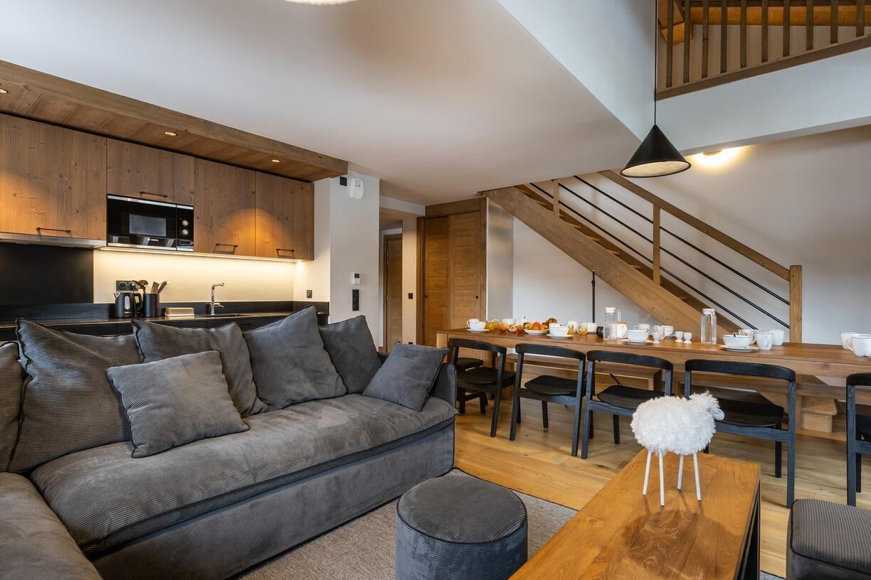 A modern living space with a sofa, dining table, and chairs. A staircase is visible in the background.
