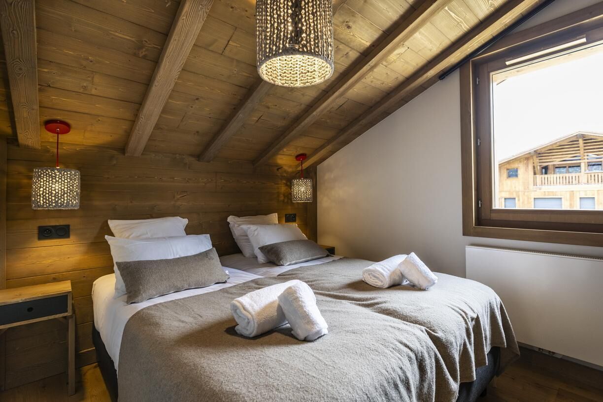 A cozy bedroom with wooden beams, two beds with towels, and hanging light fixtures.