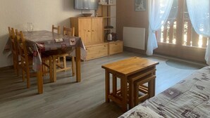 A cozy room with a wooden dining table, chairs, a small wooden stool, a TV on a wooden stand, and a bed with patterned bedding. - 350m from ski slopes, Ground floor, terrace, parking, tv, ski locker, 24m², Valloire (Valloire)