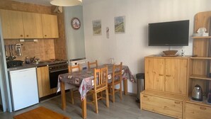 A compact kitchen with wooden cabinets, a dining table with chairs, a TV mounted on the wall, and a small wooden cabinet. - 350m from ski slopes, Ground floor, terrace, parking, tv, ski locker, 24m², Valloire (Valloire)
