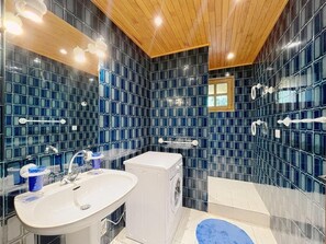 A modern bathroom with a large mirror, two sinks, a washing machine, and a shower area.