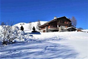 A large, multi-story building with a stone facade, surrounded by snow-covered terrain and sparse trees.