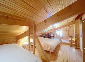 A wooden cabin with a loft bedroom, a small seating area, and a staircase.