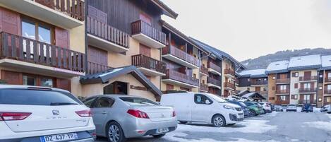 Una hilera de edificios de varios pisos con balcones, coches aparcados y suelo cubierto de nieve.