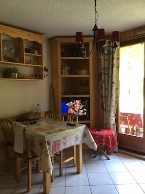 A dining area with a table set for four, wooden chairs, a chandelier, and a television on a wooden cabinet. - 350m from ski slopes, Ground floor, terrace, balcony, parking, tv, ski locker, 24m², Valloire (Valloire)