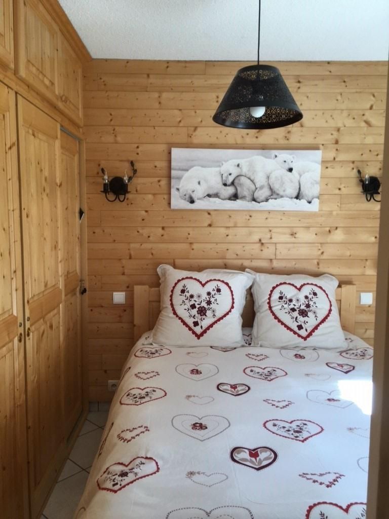 Accogliente camera in legno con un letto e lenzuola a motivi cardi, una fotografia di un orso polare appesa alla parete e una lampada a sospensione.