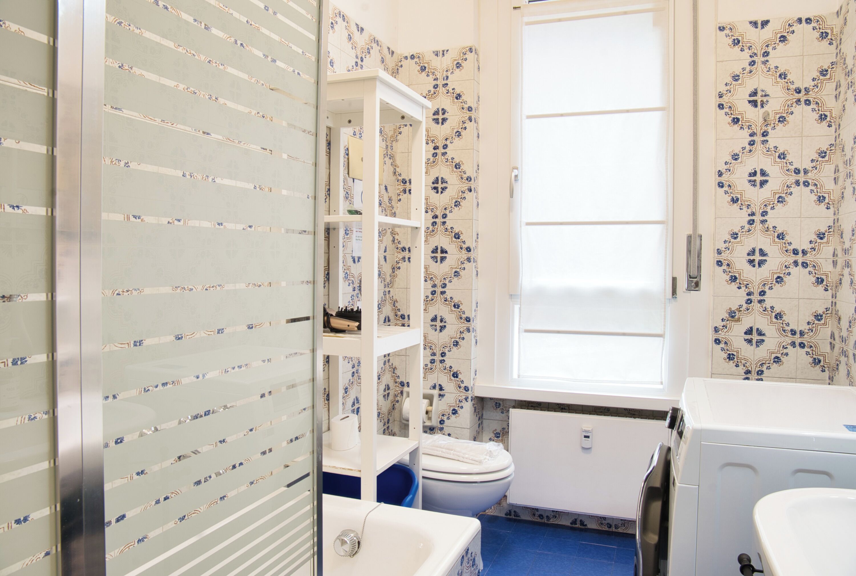 Une salle de bain avec une baignoire blanche, des toilettes et un lave-linge. Une fenêtre laisse entrer la lumière naturelle.