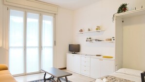 A hotel room with a bed, a sofa, a desk, a television, and a sliding door to a balcony.