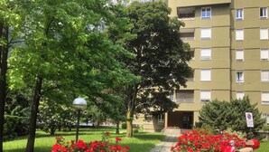 A paved pathway with red flowers, a red scooter, and a multi-story building with windows and balconies.