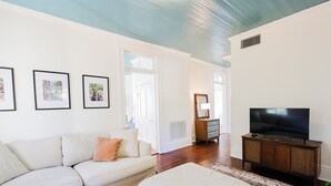 A living room with a sofa, a television on a wooden cabinet, and framed pictures on the wall. - Treehouse views in Historic Downtown Thomasville, Georgia (Thomasville)