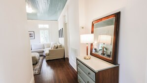 A hallway with a wooden floor, a white sofa, a dresser with a mirror, and a lamp. - Treehouse views in Historic Downtown Thomasville, Georgia (Thomasville)