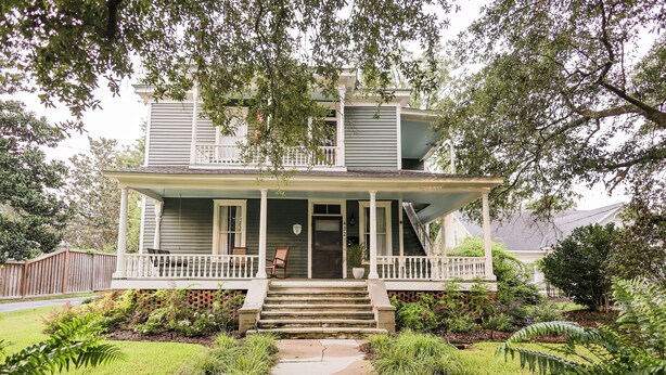 A two-story house with a front porch, a staircase leading to the entrance, and a garden with various plants. - Treehouse views in Historic Downtown Thomasville, Georgia (Thomasville)