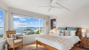 Une chambre avec une grande fenêtre, un lit, une chaise et une table de chevet.