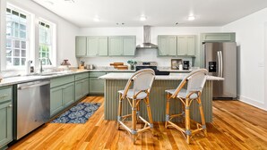 A modern kitchen with green cabinets, a stainless steel refrigerator, and two wicker bar stools. - Gorgeous Auburn Getaway! BRAND NEW 3Bed/3Bath (Auburn)