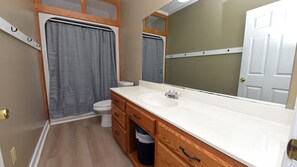 Un baño pequeño con lavamanos blanco, tocador de madera y ducha con cortina gris.