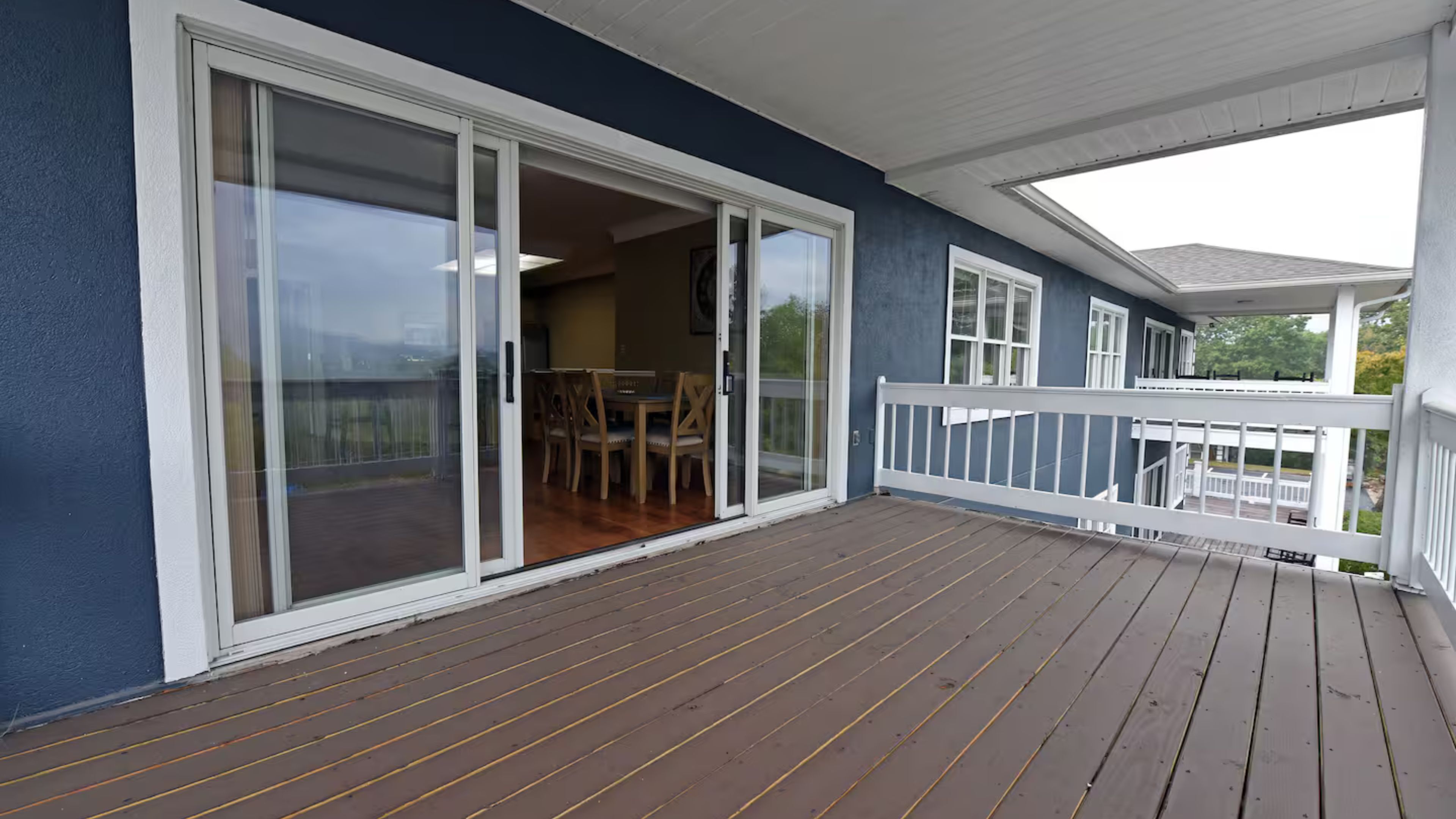 Une terrasse en bois couverte, avec une porte vitrée donnant accès à un espace intérieur comprenant une table et des chaises.