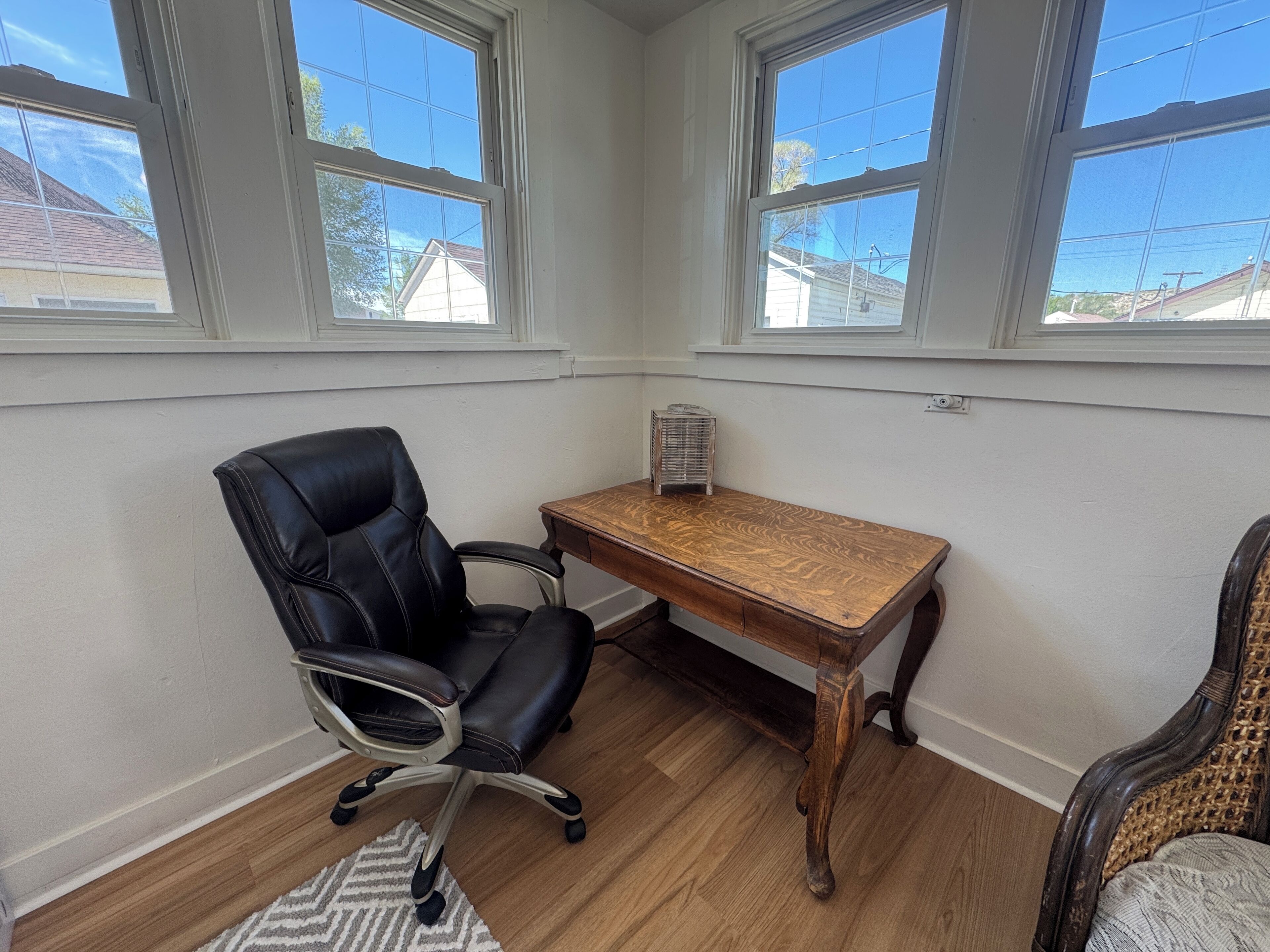 Une pièce avec un bureau en bois, un fauteuil de bureau noir et une chaise en osier.