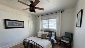A bedroom with a bed, a chair, a ceiling fan, a window, and a door.