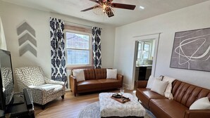 A living room with a brown leather sofa, a patterned armchair, a coffee table, and a ceiling fan.