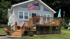 A two-story house with a wooden deck, a balcony with red flowers, and an American flag.