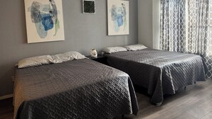 A hotel room with two beds, a ceiling fan, artwork on the walls, and a window with curtains.