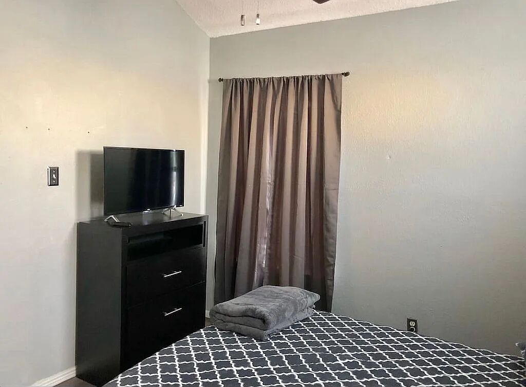 Un dormitorio con una cama, un televisor sobre una cómoda y una cortina.