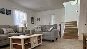A living room with two grey sofas, a white coffee table, wicker baskets, and a staircase leading to a door. - Southern Dunes- Lake View Villa -Private Pool (Haines City)