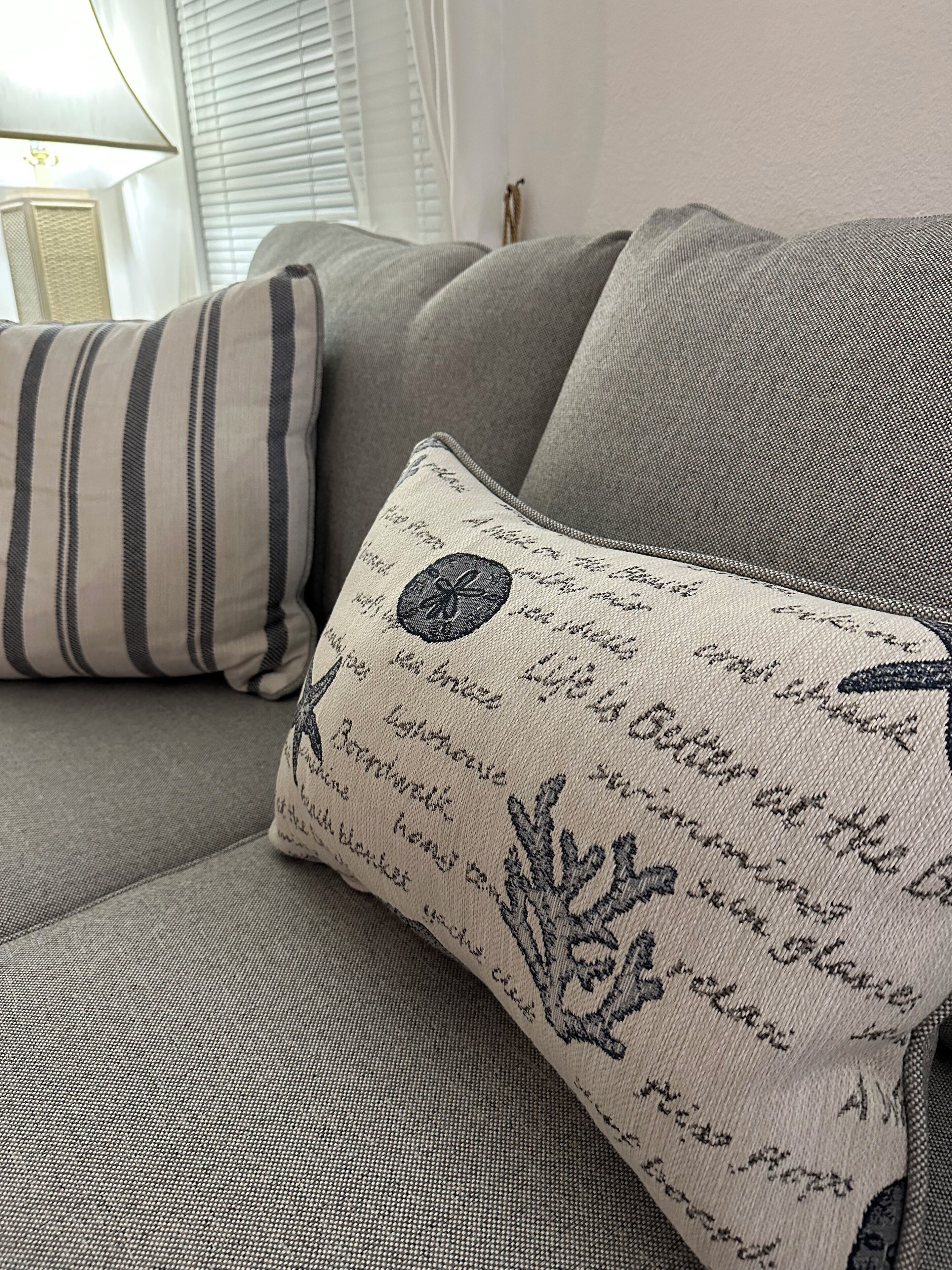 A grey sofa with two pillows, one striped and one with a leaf pattern.