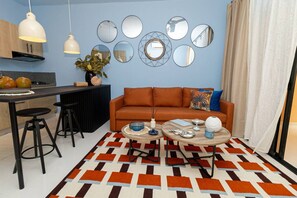 Una sala de estar moderna con un sofá, dos mesas de centro y una cocina con mesa de comedor y taburetes de bar.