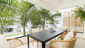 Un espace repas moderne avec une table sombre, des chaises en osier et une vue sur un jardin luxuriant agrémenté de palmiers.