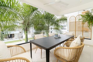 Ein moderner Essbereich mit dunklem Tisch, Korbstühlen und Blick auf einen üppigen Garten mit Palmen.