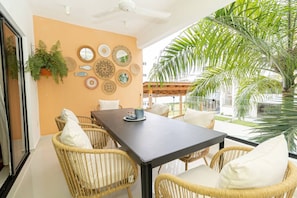 A dining area with wicker chairs, a dark table, and a wall decorated with various mirrors and woven items.