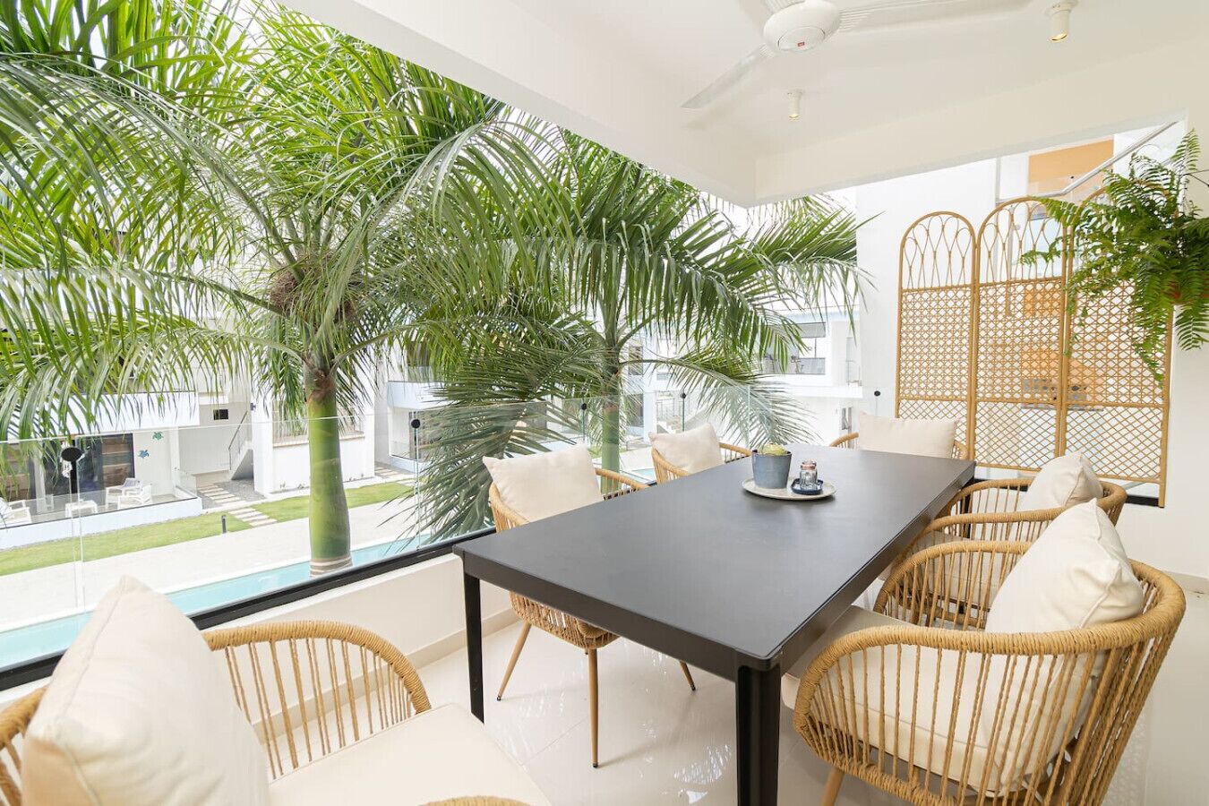 Un comedor moderno con una mesa larga, sillas de mimbre y vistas a una piscina y vegetación exterior.