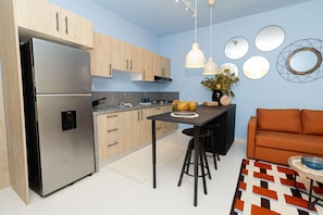 A modern kitchen with a stainless steel refrigerator, wooden cabinets, a central island with stools, and a blue wall with circular mirrors.