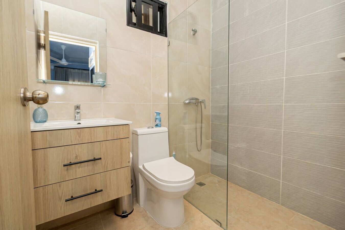Un baño moderno con tocador de madera, inodoro blanco, cabina de ducha de cristal y espejo sobre el lavabo.