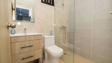 Un baño moderno con tocador de madera, inodoro blanco, cabina de ducha de cristal y espejo sobre el lavabo.
