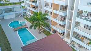 A modern multi-story hotel with a rooftop pool, outdoor seating, and a palm tree.