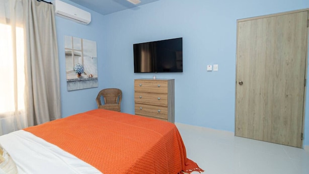 Une chambre à coucher avec un lit, une commode en bois, un téléviseur et une porte.