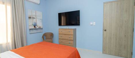 A bedroom with a bed, a wooden dresser, a television, and a door.